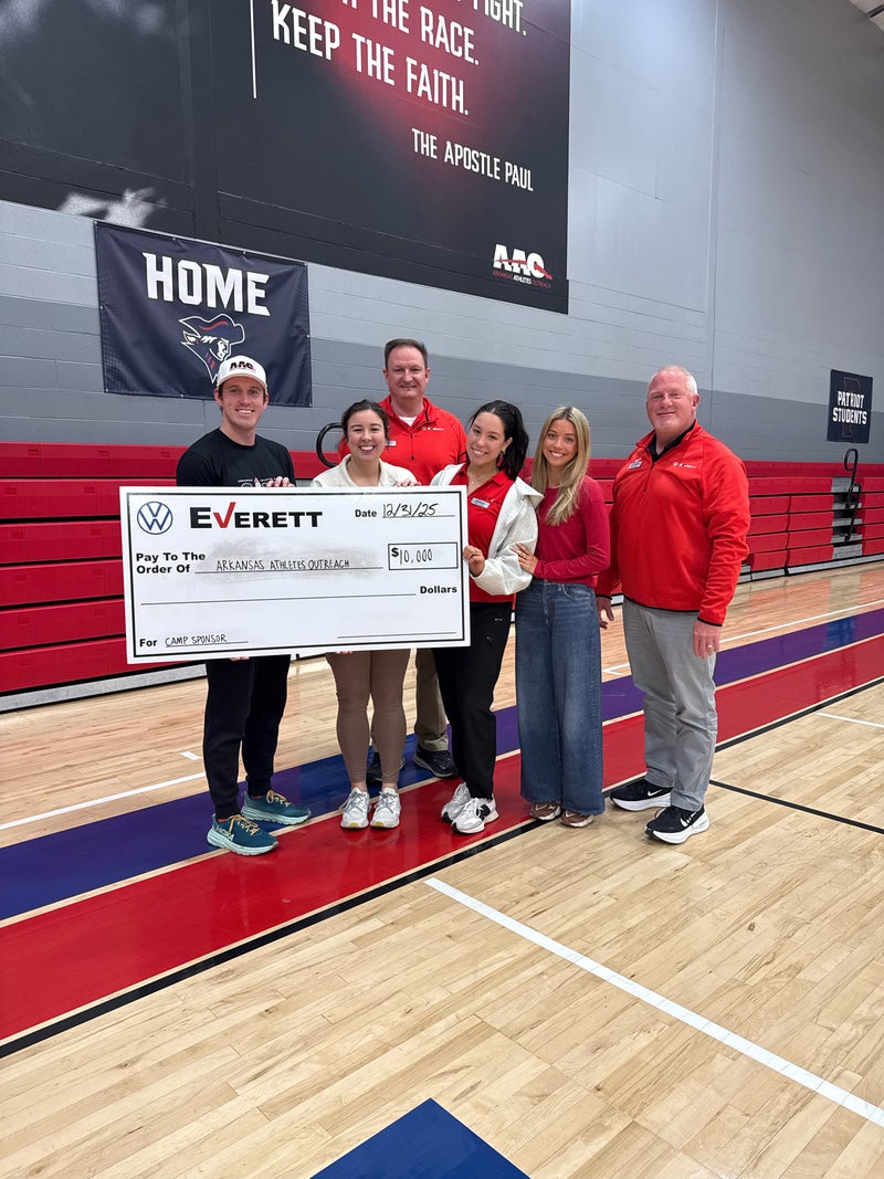 Six people, three men and three women, holding a large check for $10,000 to Arkansas Athletes Outreach