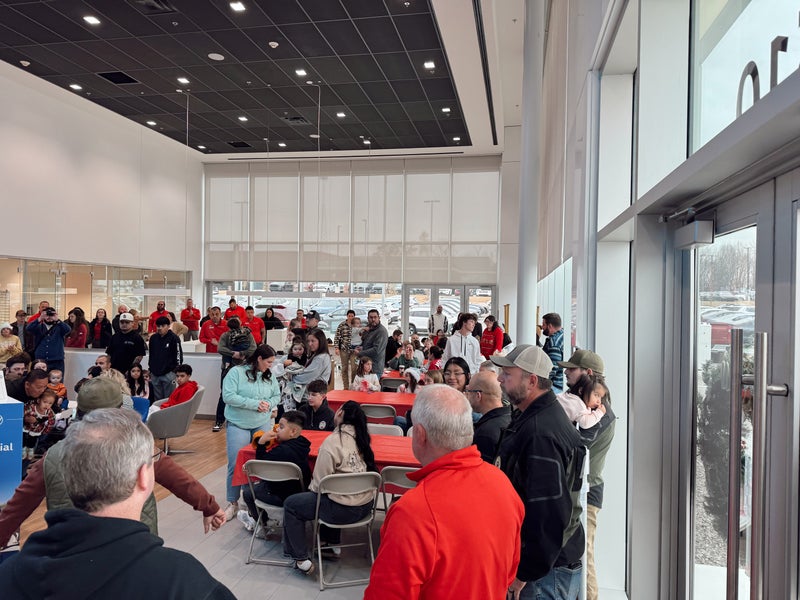 A large group of adults and children gathered in a brightly lit indoor space with modern decor, some sitting at tables